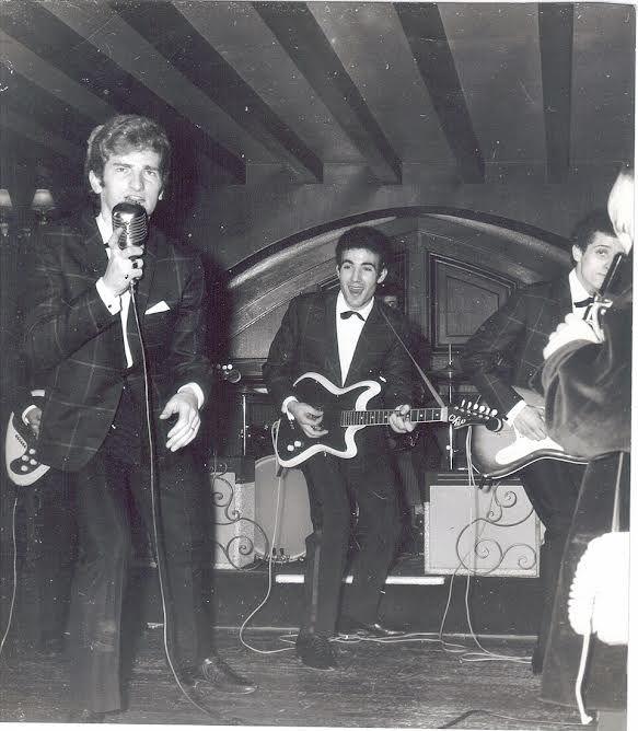 Eddy Mitchell chantant sur scène avec ses musiciens, photographie en noir et blanc.